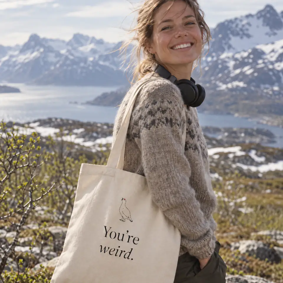 A smiling woman on a Norwegian mountain carrying the You’re weird. tote