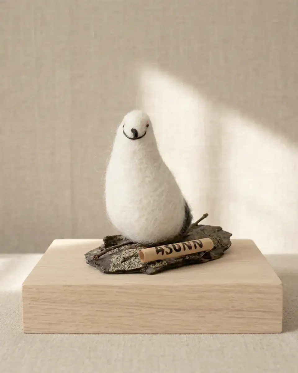 AWEBO on Rock — a hand-felted wool ptarmigan on its bark-and-stone base, on a pale oak plinth.